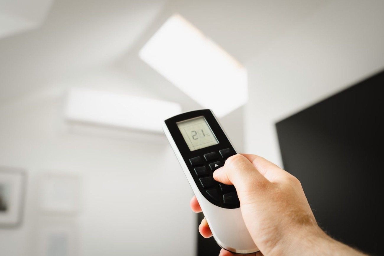 Main réglant une climatisation à 21 degrés avec la télécommande